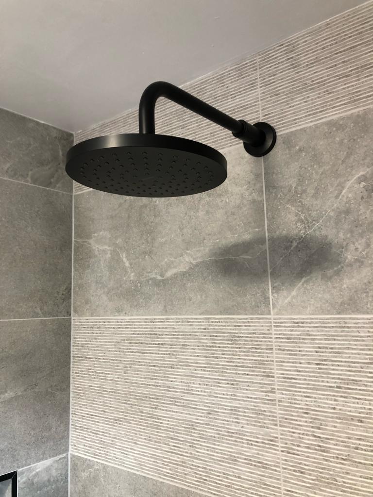 Matt black round rain shower head against grey marble-effect tiles