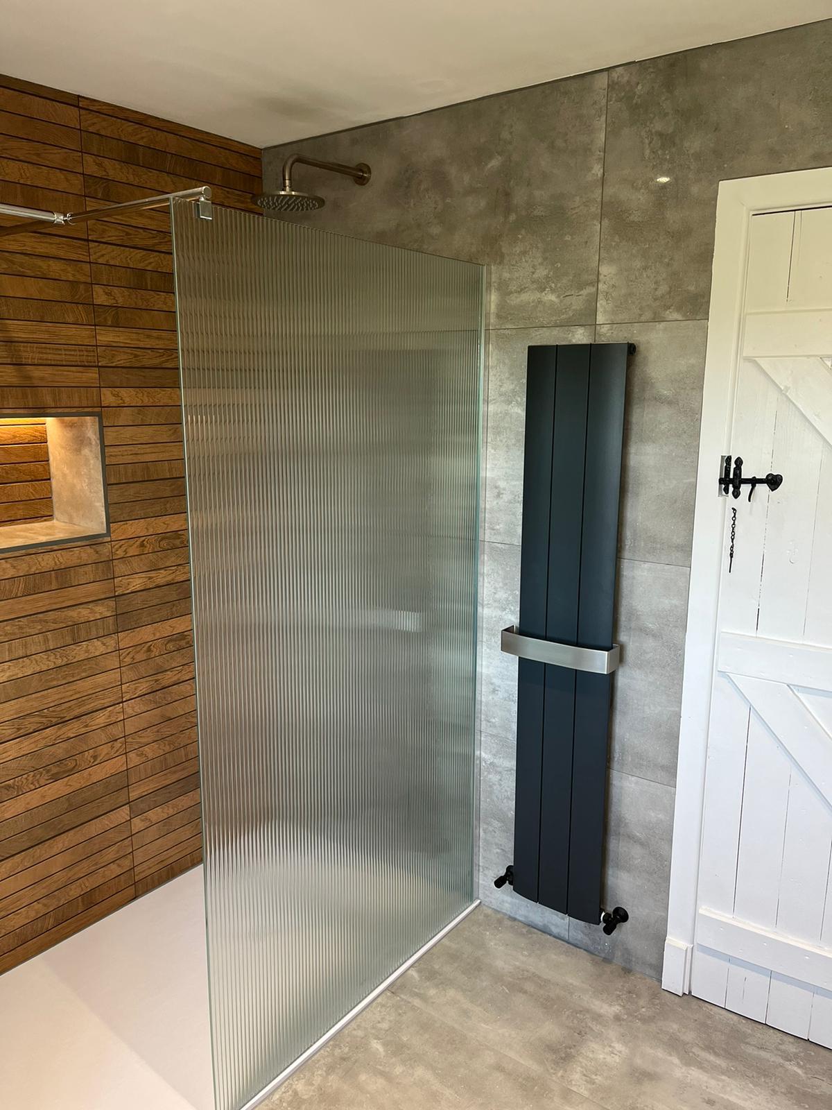 Reeded glass shower screen beside an anthracite vertical radiator and concrete-effect tiling