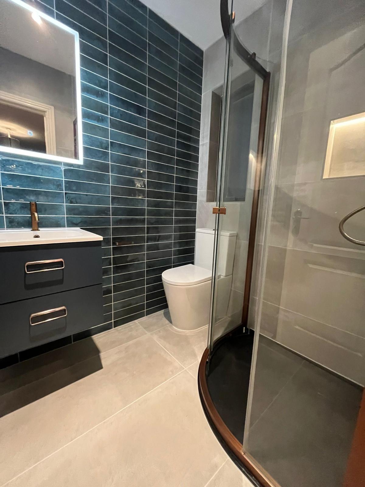 Full view of the teal and grey bathroom with quadrant shower enclosure and copper-trimmed frame