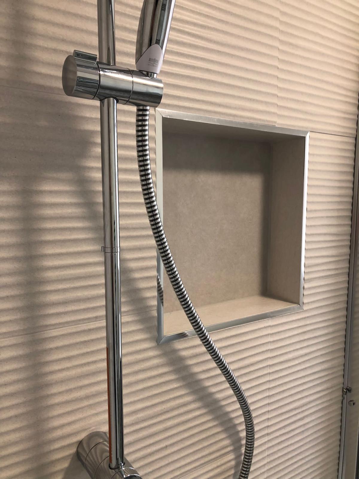 Chrome-trimmed shower niche and riser rail set against textured ripple wall tiles