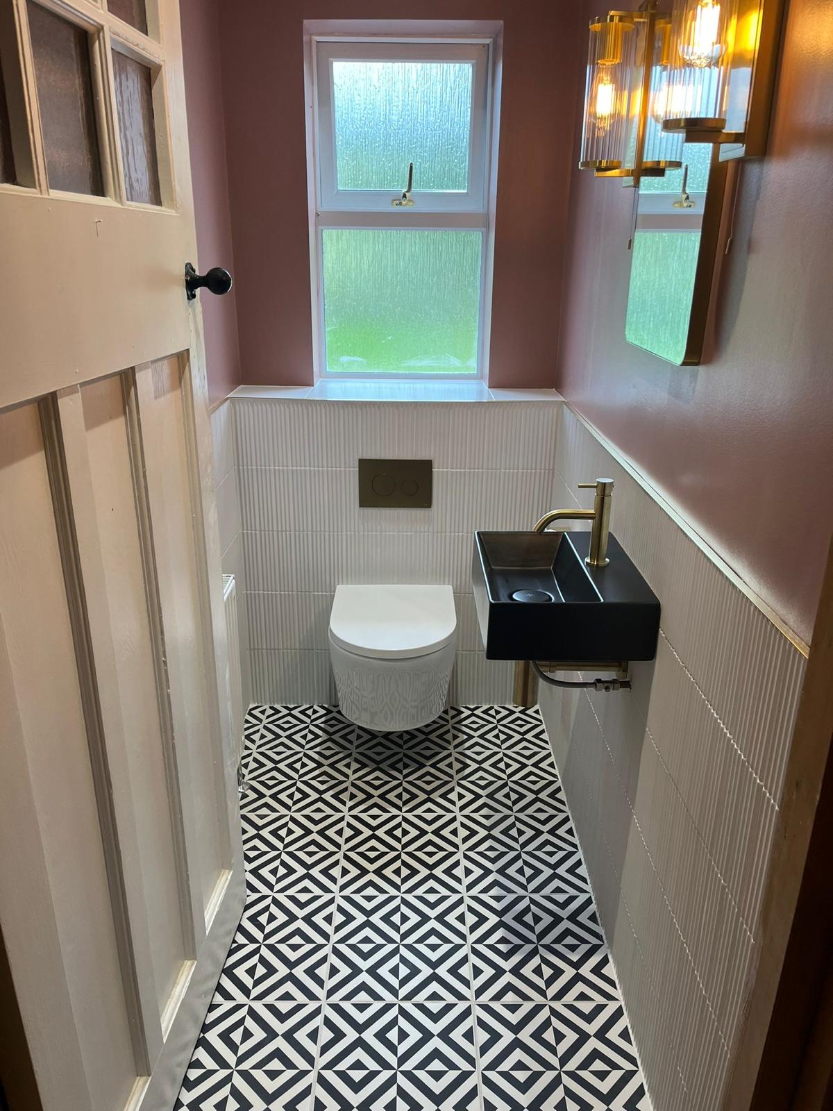 Matt black wall-hung basin with brushed brass tap above a geometric monochrome floor