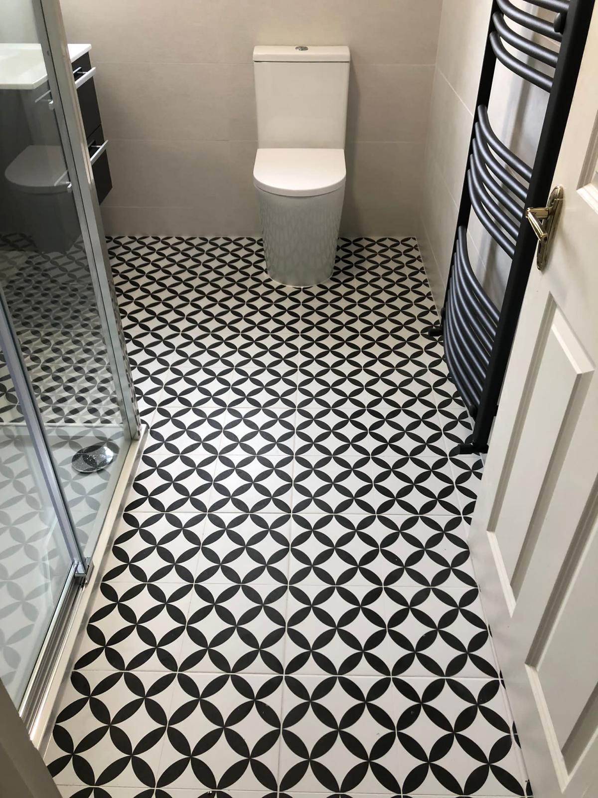 Black and white geometric floor tile running through the shower room to a rimless WC and chrome towel radiator