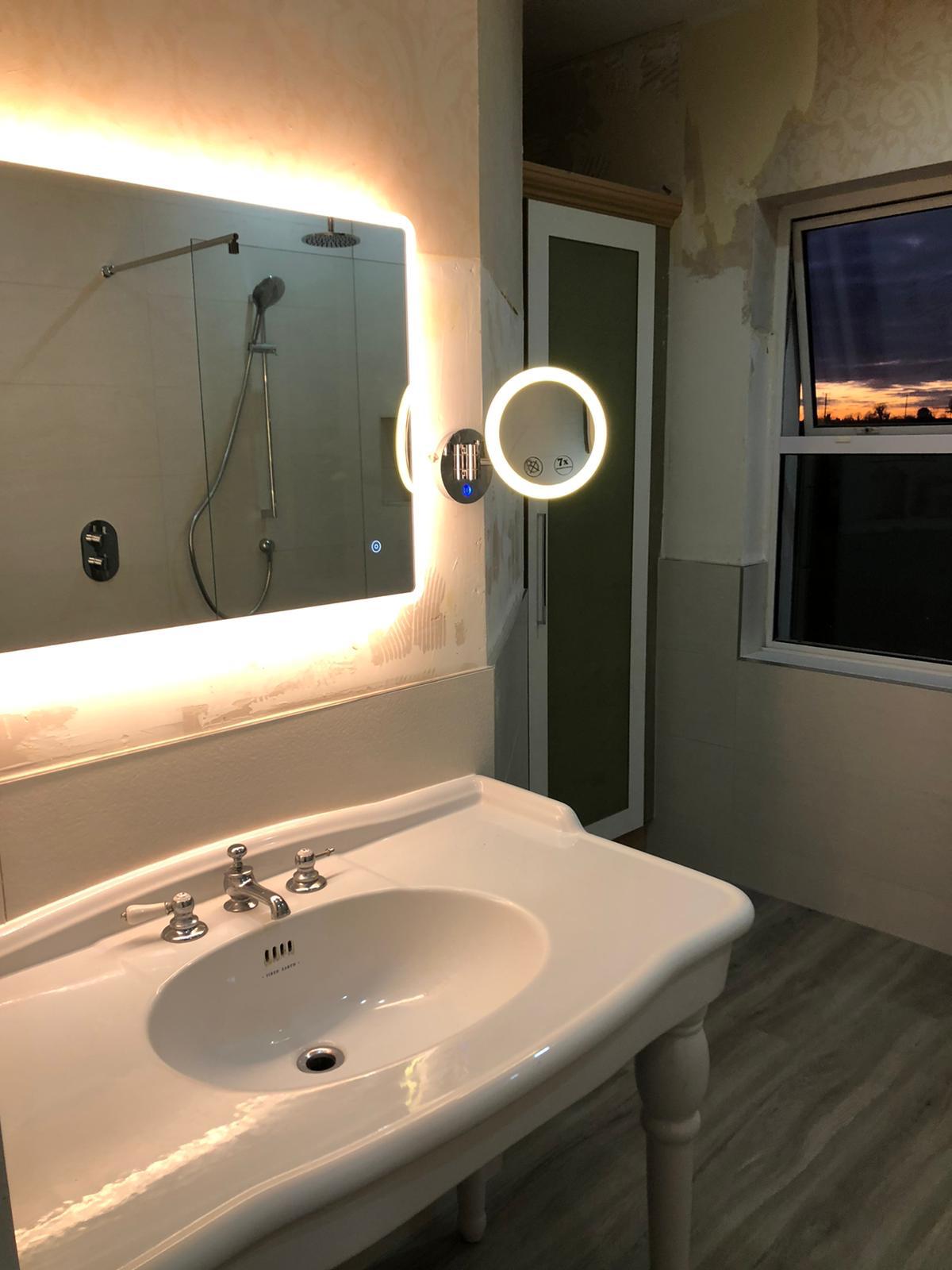 Traditional console basin on turned legs beneath a backlit mirror and magnifying light