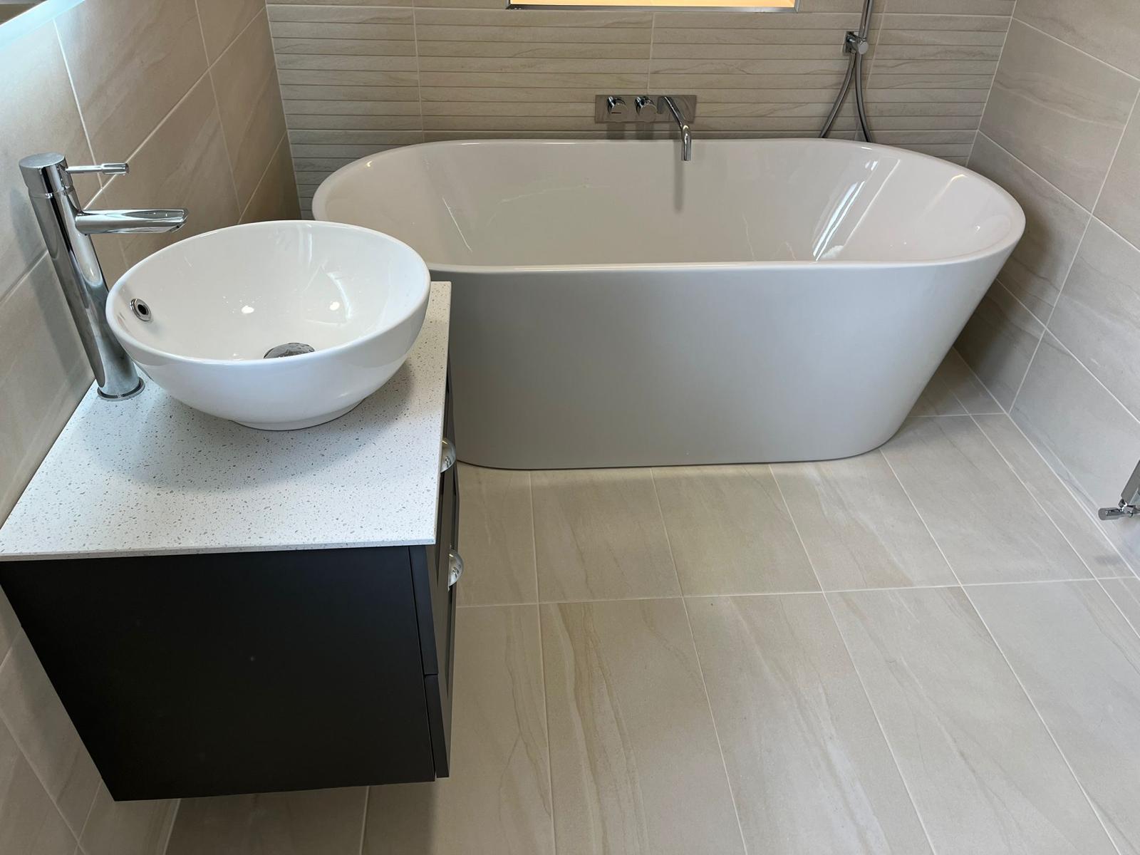 Freestanding bath beside a graphite vanity with counter-top bowl basin, fitted by Plan B