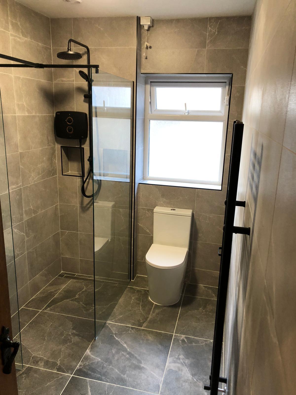 Level-access wet room with frameless glass screens, matt black rain shower and stone-effect porcelain
