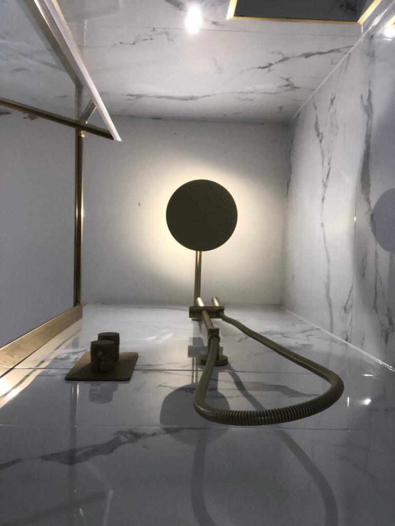 Brass rain shower head lit against a marble-lined shower enclosure