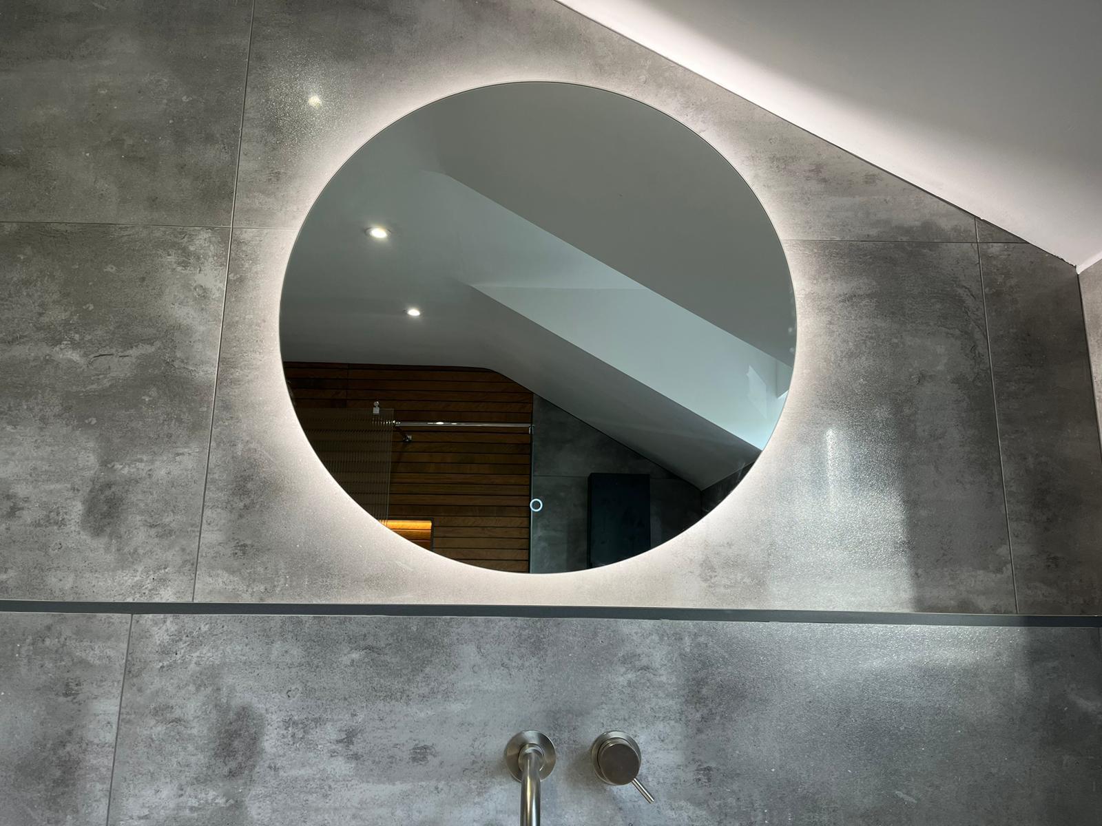Backlit circular mirror set into concrete-effect porcelain wall tiling