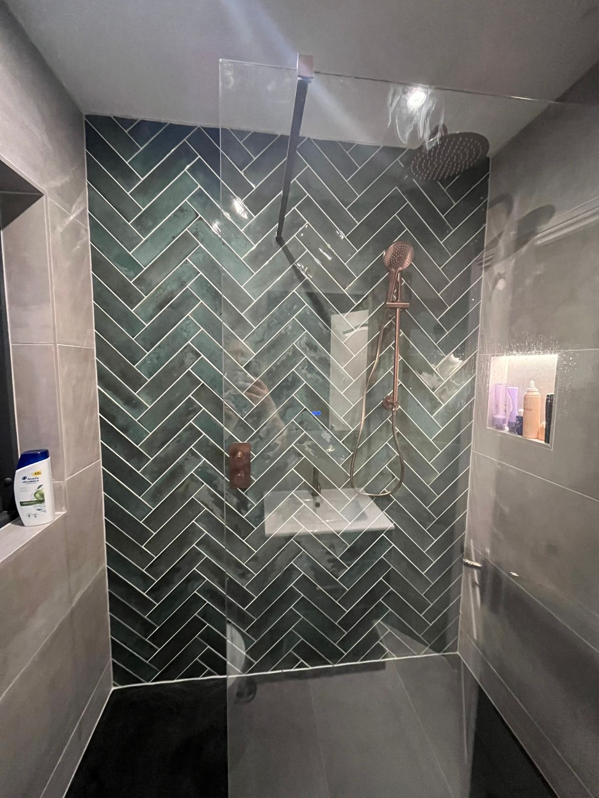 Teal herringbone shower feature wall with brushed copper rain head, handset and lit niche