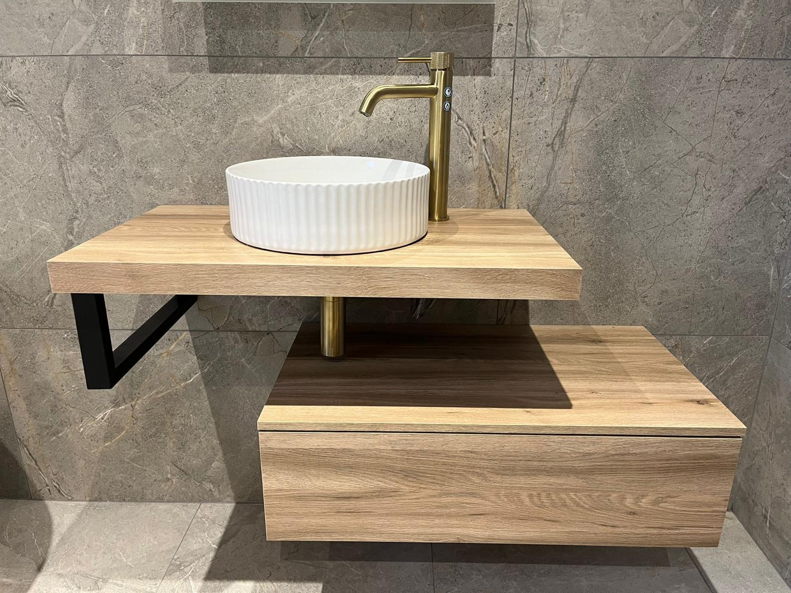 Two-tier oak vanity detail with black bracket and brass bottle trap