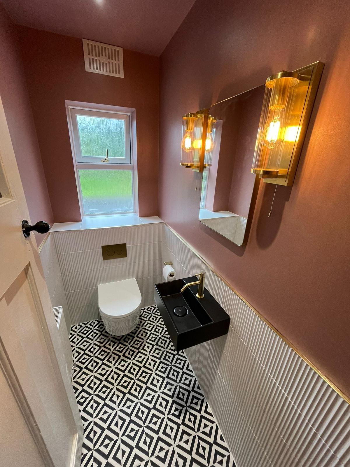 Cloakroom with monochrome patterned floor, fluted white tiling, rose walls and brass wall lights