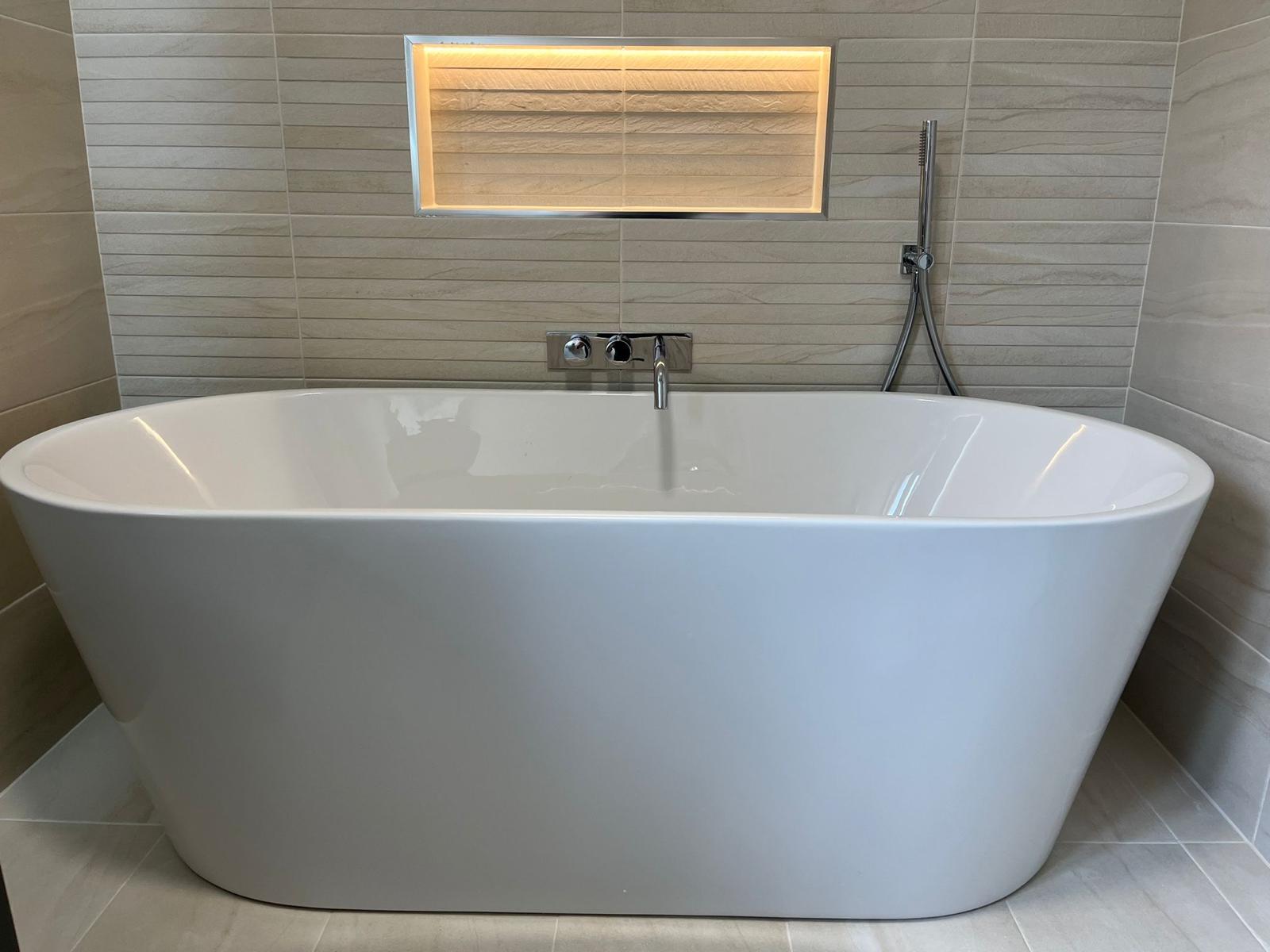 Freestanding bath with wall-mounted chrome filler and an LED-lit recessed stone niche