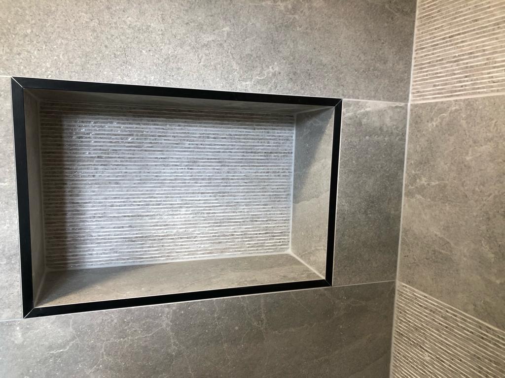 Recessed shower niche framed in matt black and lined with ribbed stone tile