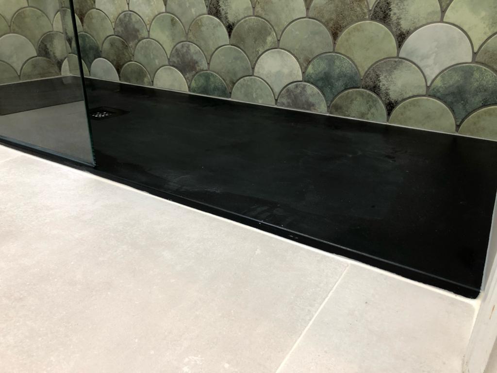Slimline black shower tray set flush with pale stone-effect floor tiles