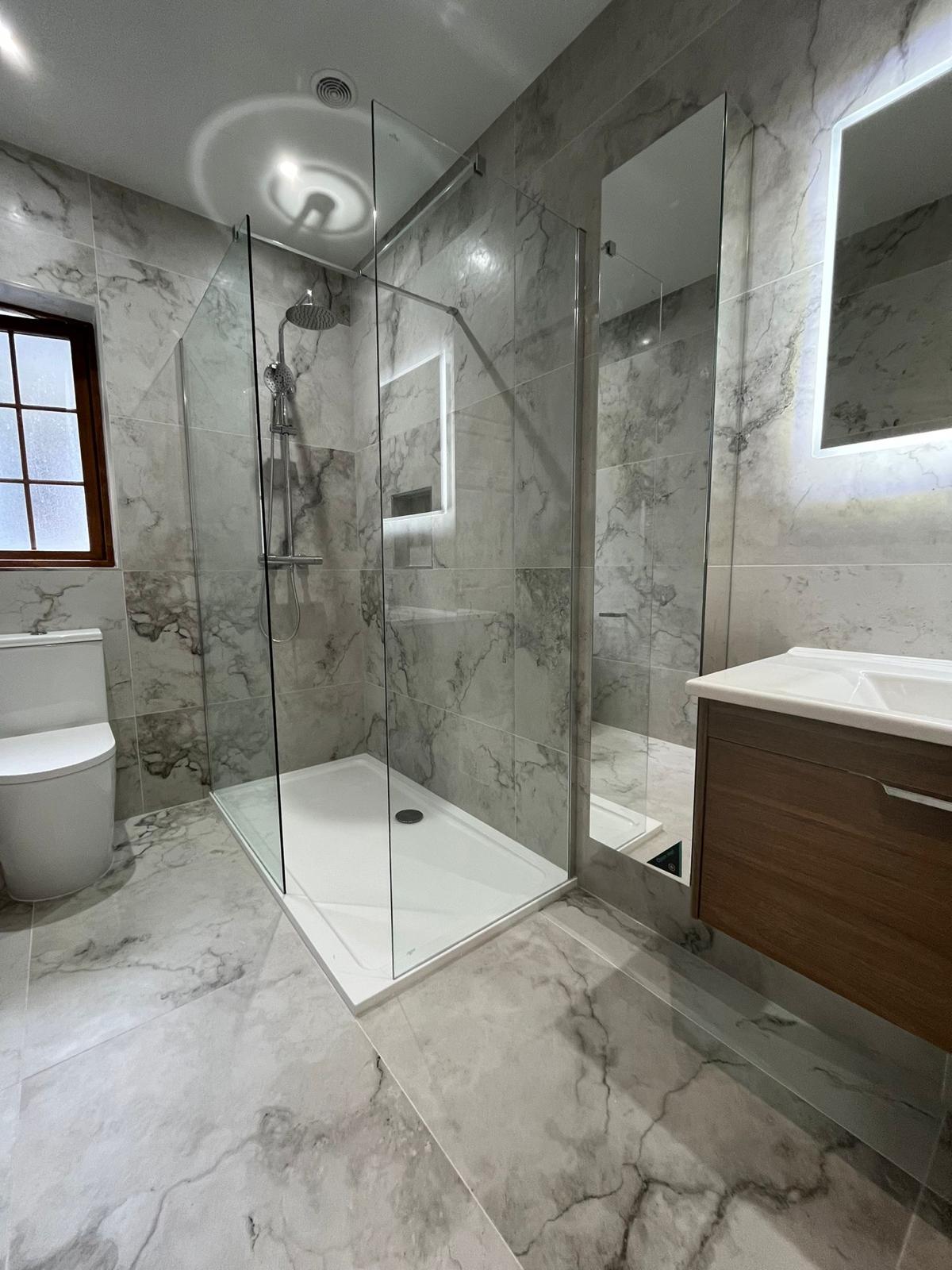Level-access walk-in shower with frameless screen, lit niche and grey marble-effect porcelain