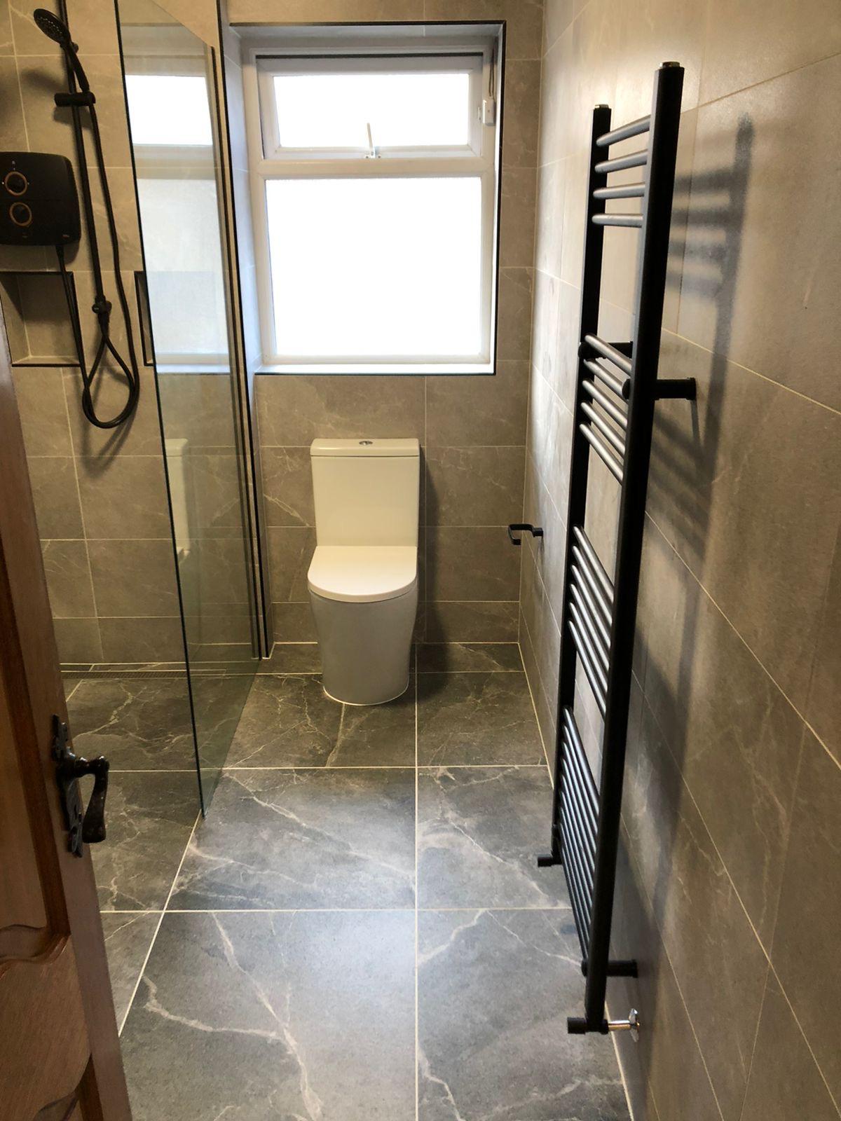 Wet room view showing close-coupled WC, black ladder radiator and glass shower screen