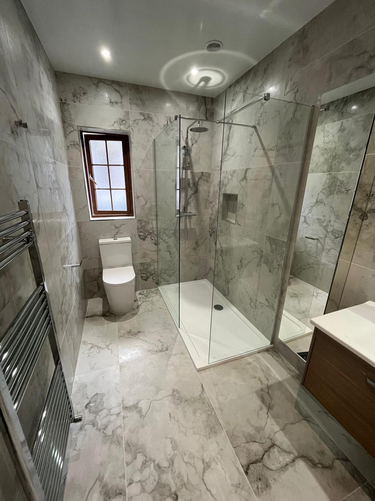 Walk-in shower, chrome ladder radiator and walnut wall-hung vanity in a grey marble bathroom