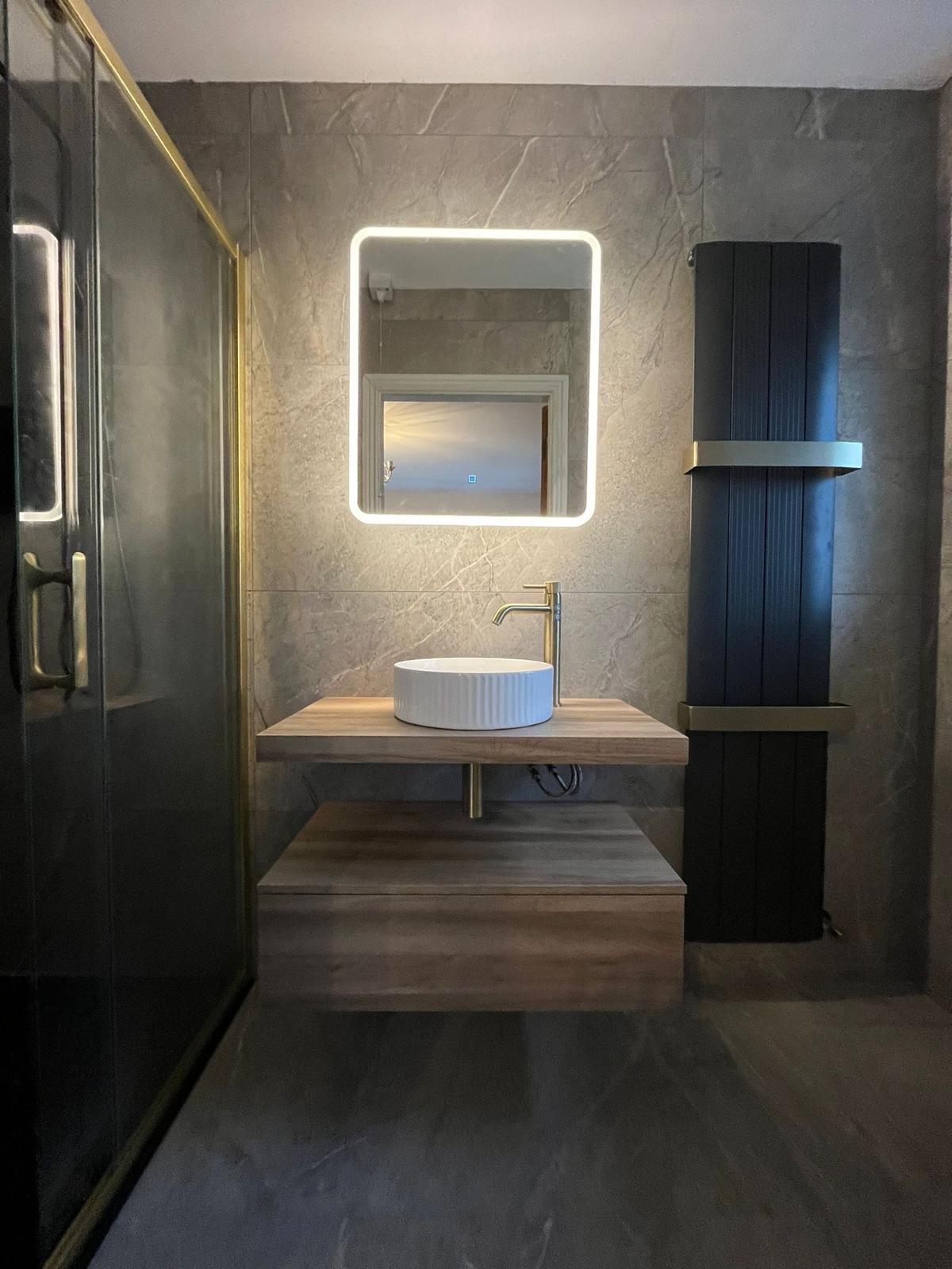 Backlit mirror above the vanity with brass-framed shower enclosure