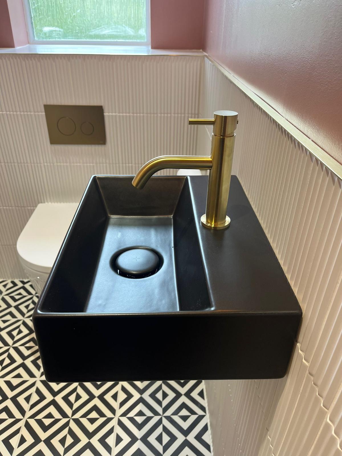 Close-up of the matt black basin, brushed brass tap and brass flush plate
