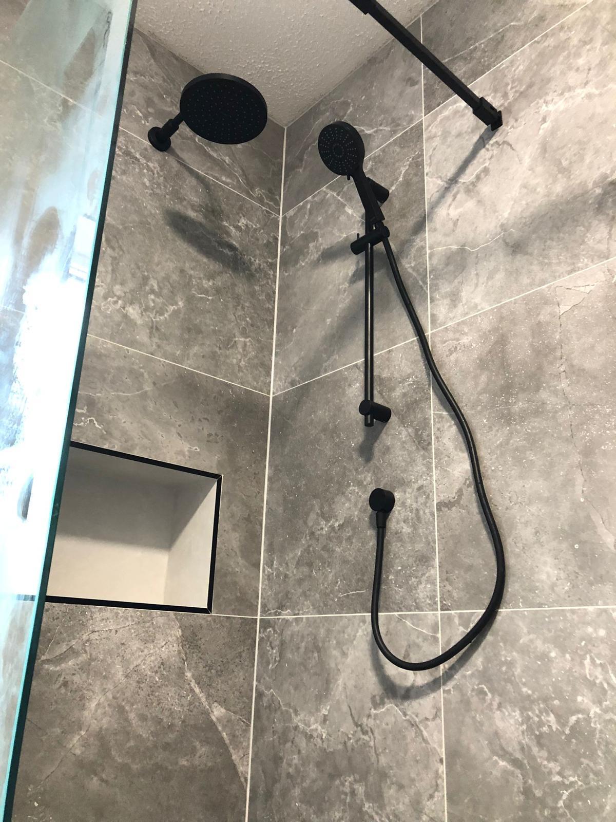 Matt black rain head, riser rail and handset against grey marble-effect tiling with a black-trimmed niche