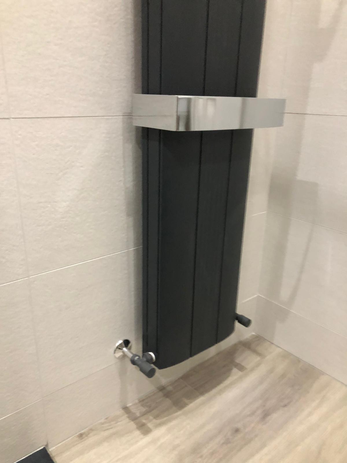 Anthracite vertical designer radiator with a chrome towel shelf against linen-effect tiling
